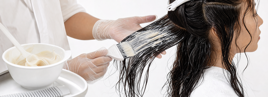 Profissional aplicando tratamento proteico por mechas em cabelo longo dentro de um salão iluminado