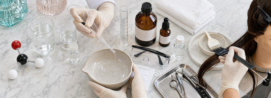 Frasco de laboratório ao lado de modelo molecular do formaldeído, mecha de cabelo, luvas e prancha capilar sobre bancada clara