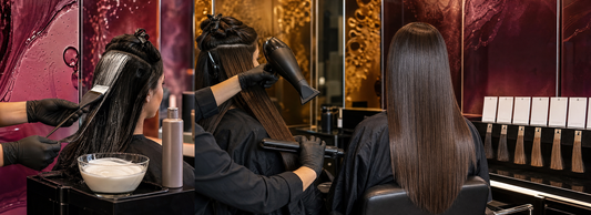 Cabeleireira avaliando uma mecha de cabelo alinhado ao lado de produtos capilares, luvas, secador e prancha em bancada de salão